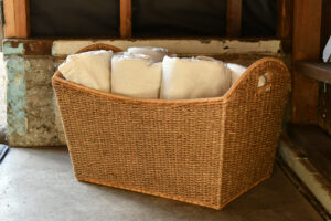 A weaved basket containing linens resting on a concrete slab with unfinished framed walls in the background.