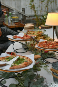 Several different artisan pizzas with eucalyptus branches laying underneath their trays.