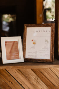Two picture frames resting on a wooden shelf with a dark background. The picture frames display shuttle times and a drink menu.