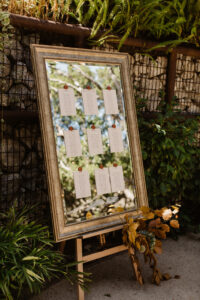 A framed mirror resting on an art easel with seating arrangements printed on small papers being held on by magnets.